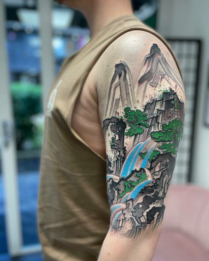 A vibrant forearm tattoo art of a mountain landscape with waterfalls and green trees, an inspiring tattoo art example.