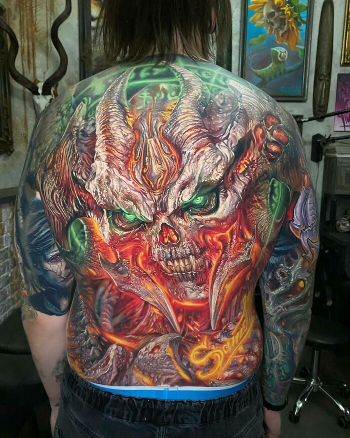 An intricate back tattoo art of a fiery, demonic skull with glowing green eyes, an inspiring example of tattoo art.