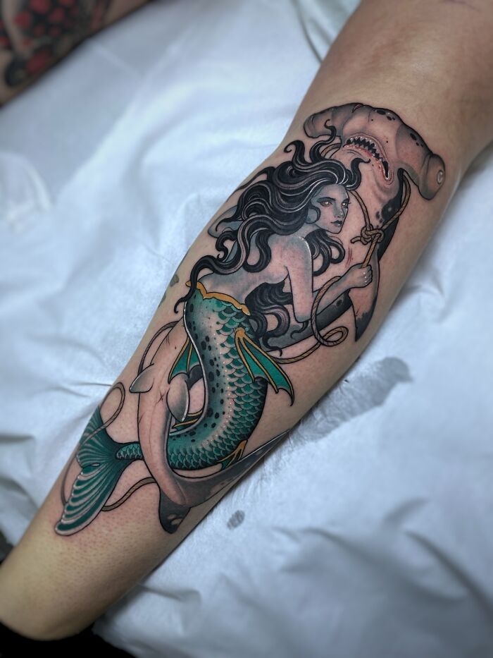 A detailed calf tattoo art depicting a mermaid holding an anchor with a hammerhead shark, a unique tattoo art example.