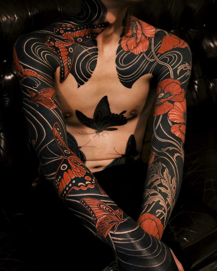 Full body tattoo art of black and red butterflies and flowers on a person's chest and arms, showcasing inspiring tattoo art.