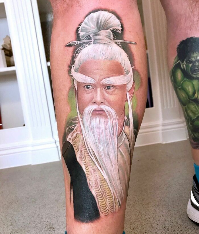 Detailed leg tattoo art portrait of a character with white hair and beard, an inspiring example of tattoo art.