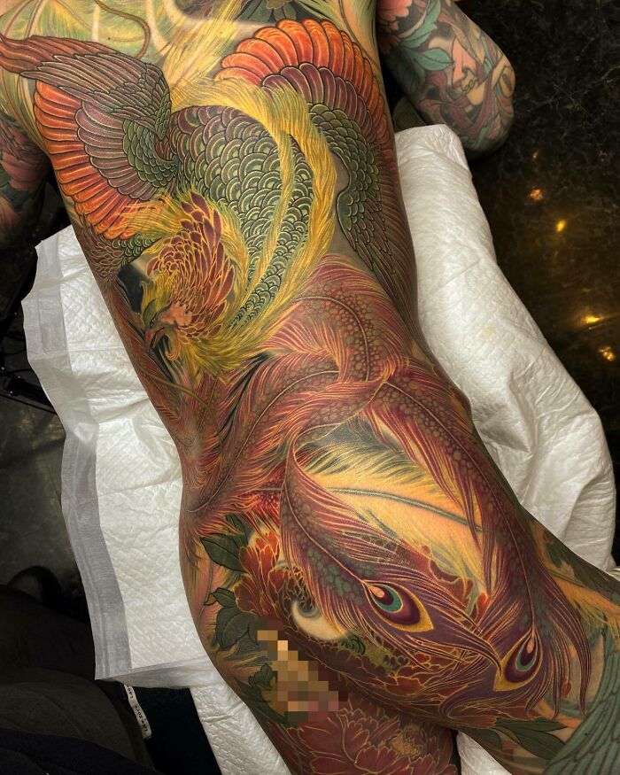 An elaborate full body tattoo art of a majestic phoenix with richly colored feathers, a stunning example of inspiring tattoo art.