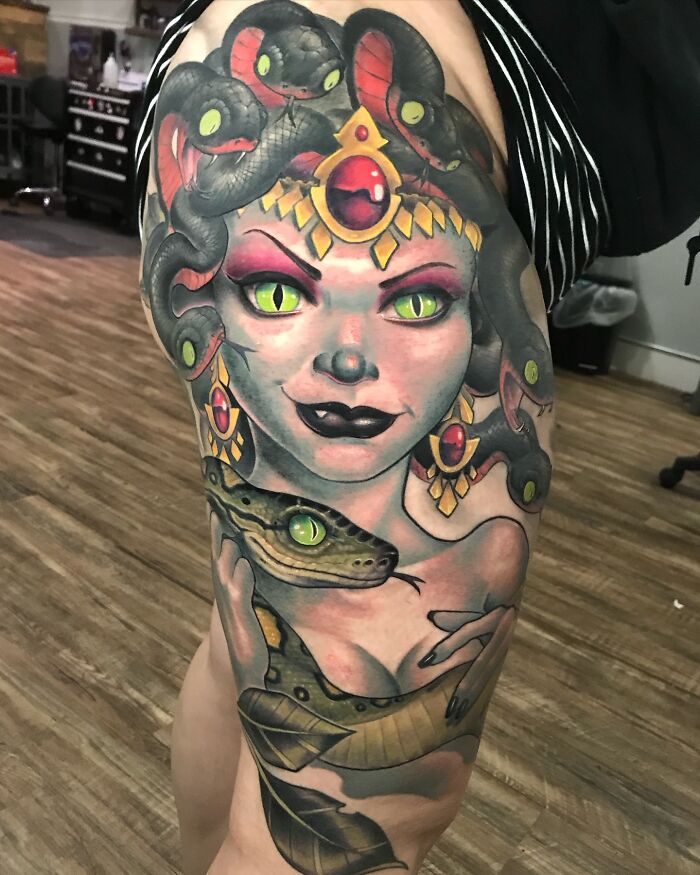 A vibrant Medusa tattoo art with glowing green eyes and snakes on a thigh, showcasing detailed tattoo art.