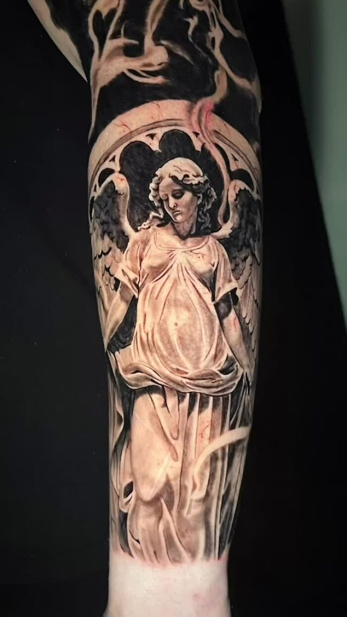 Realistic black and grey tattoo art of an angel statue on an arm, a compelling example of tattoo art.