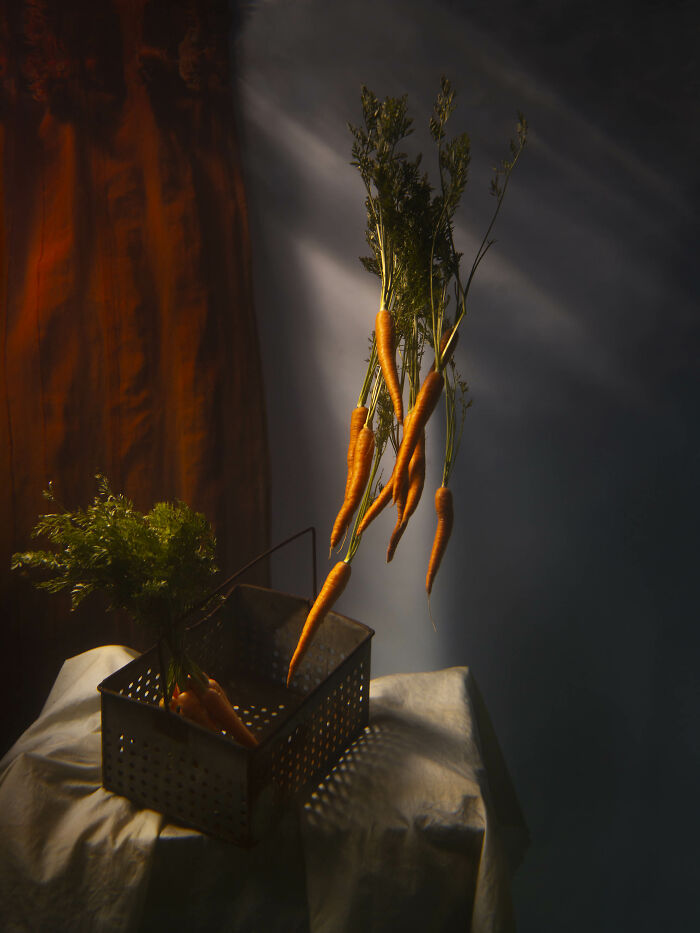 Surreal photos of carrots appearing to float above a metal basket and white cloth, against a dark background.