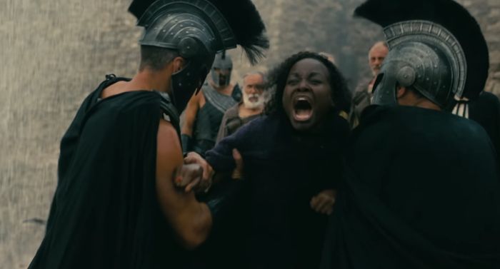 A woman screaming as two men in Spartan helmets hold her. This image is related to The Odyssey film adaption.