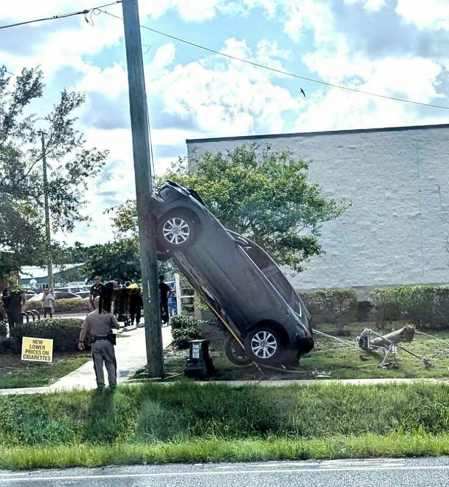 A black car is parked vertically on a utility pole, showing a rough day behind the wheel.