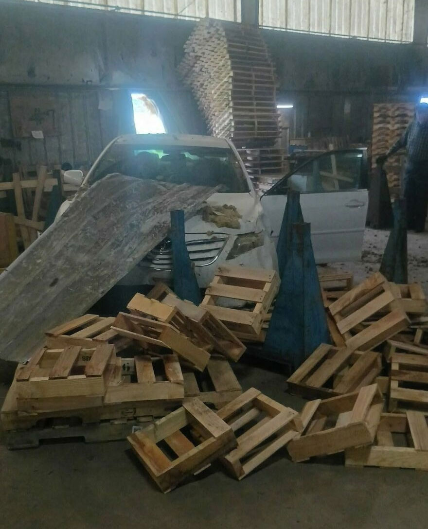 A car crashed into a stack of wooden pallets in a warehouse, a rough day behind the wheel.