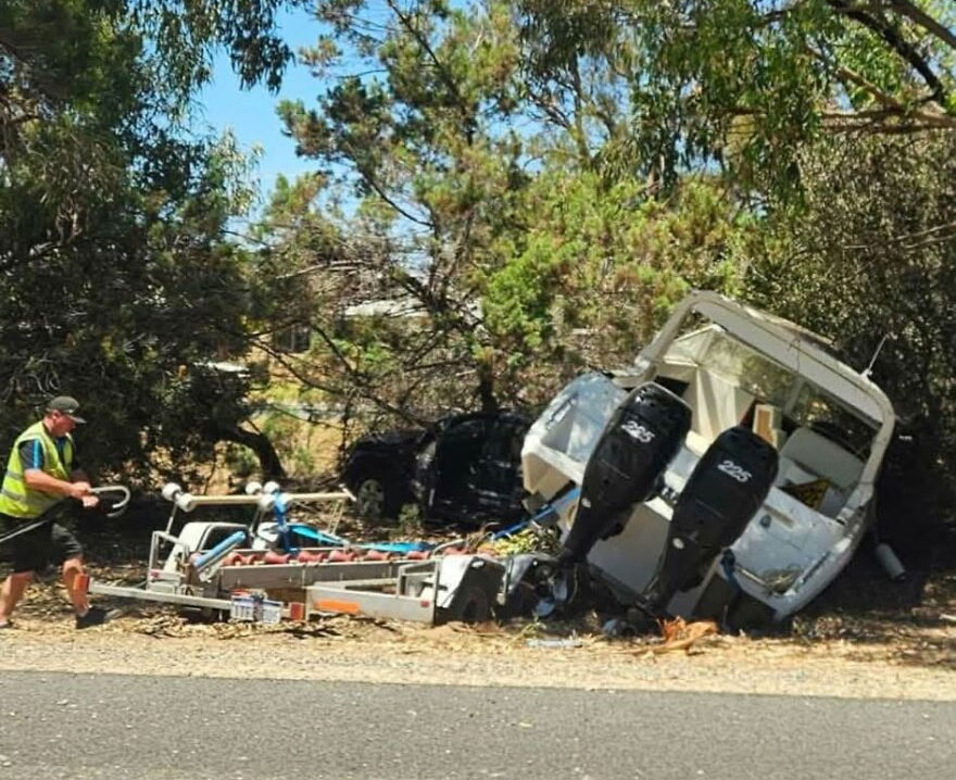 A boat trailer and boat are overturned by the roadside, a rough day behind the wheel.