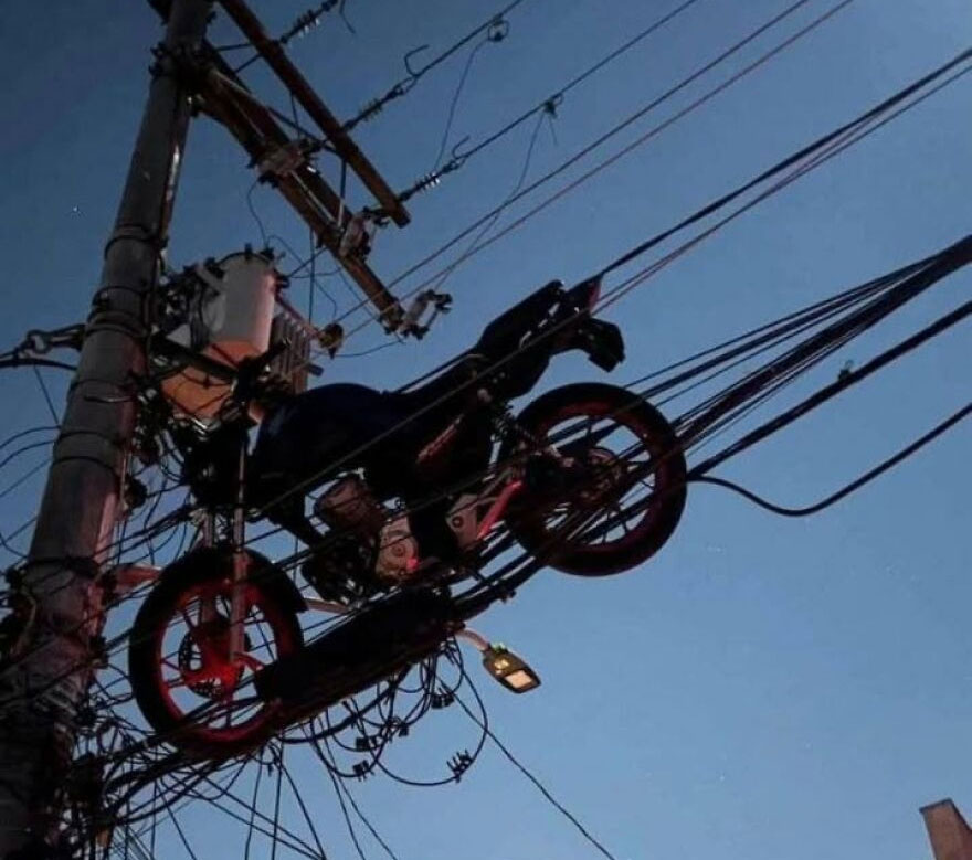 A motorcycle suspended in power lines, showing a rough day behind the wheel and an ironic parking spot.