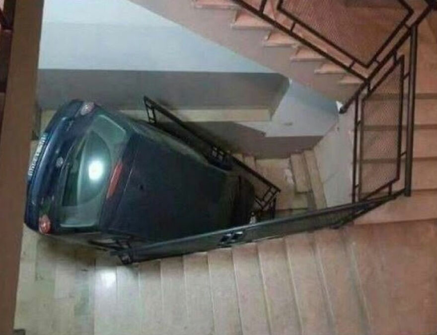 A small car fallen down a flight of stairs in a building, creating a difficult parking situation.