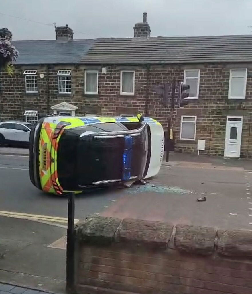 An overturned police car lying on its side on a road with broken glass scattered nearby, a rough day behind the wheel.
