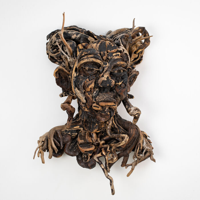 A stunning sculpture of a dark-colored human bust, crafted from collected pieces of wood against a white background.
