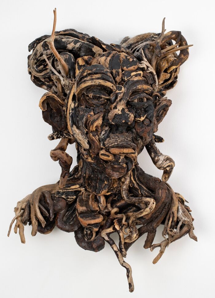 A stunning sculpture of a dark-colored human bust, crafted from collected pieces of wood against a white background.