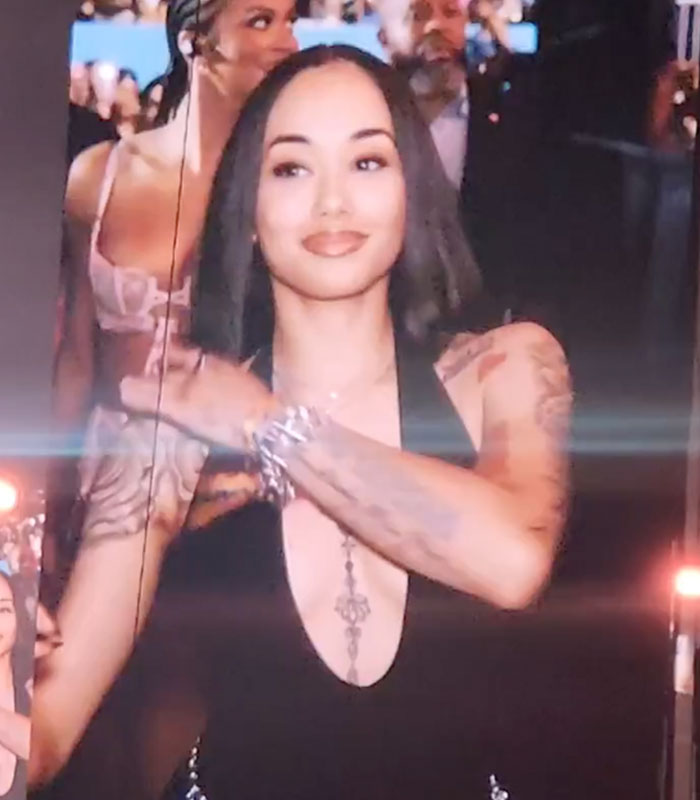 A woman with long dark hair and tattoos on her arms, looking at the camera with a slight smile.