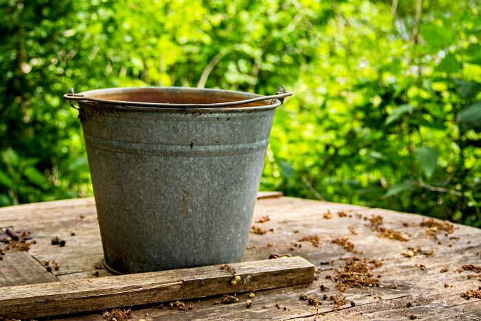 An old metal bucket on a wooden table outdoors, something guests might notice in someone's home.