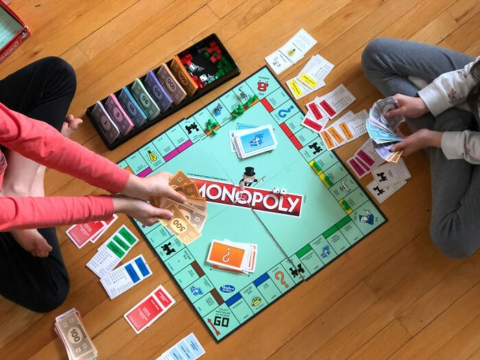 Guests playing Monopoly on a wooden floor, showing a fun activity within someone's home.