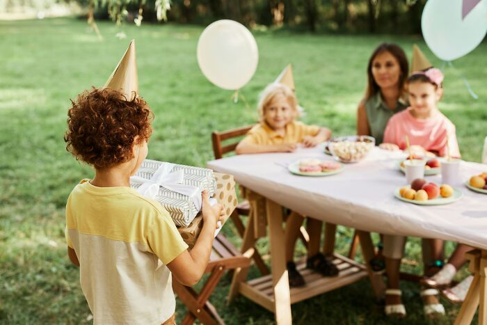 A child holding a gift at an outdoor birthday party, making guests feel welcome in someone’s home.