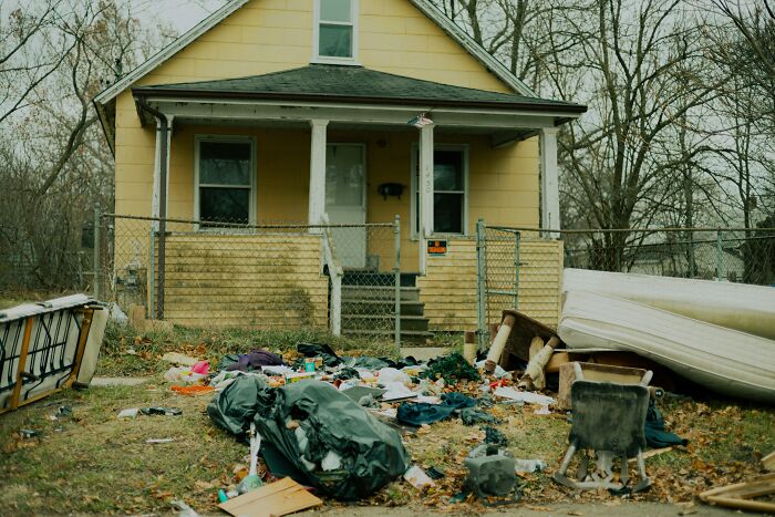 A dilapidated yellow house with trash and debris scattered in the front yard, suggesting a guest would never return.
