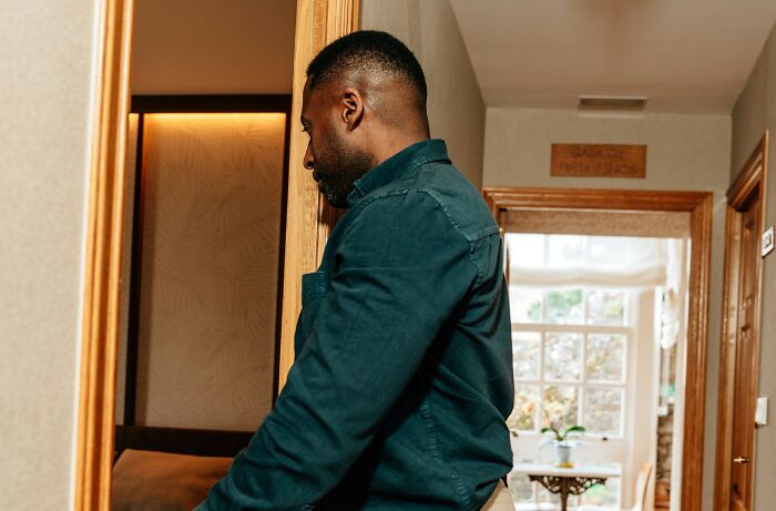 A man looking into a mirror in a dimly lit hallway, reflecting suspenseful babysitting stories.