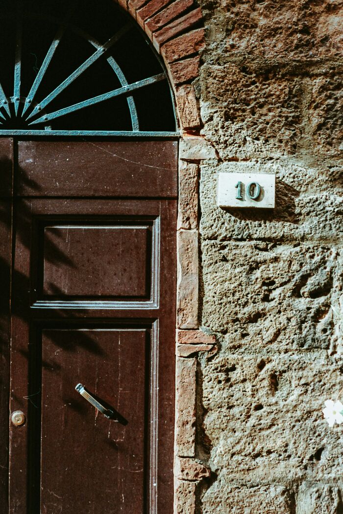An ancient, weathered wooden door with an ornate arch and a rustic number 10, highlighting mansplaining.