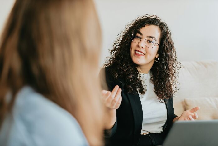 A woman with curly hair and glasses talking to another person, discussing psychological red flags.