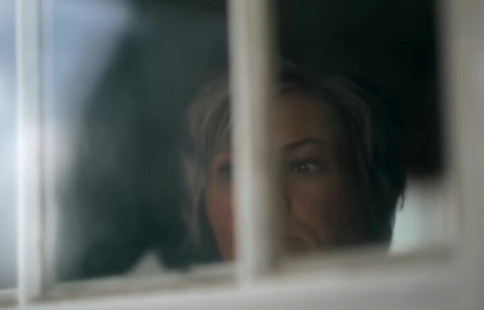 A woman looking intently through a window, possibly observing the worst neighbor ever.