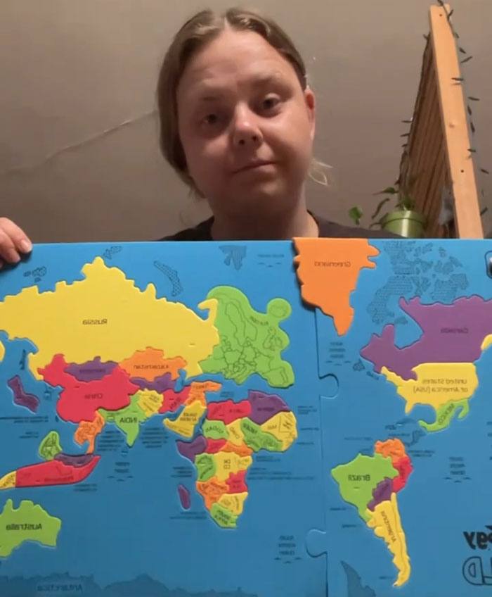 A woman holding up a colorful world map puzzle, demonstrating the actual scale of the continents compared to common perceptions.