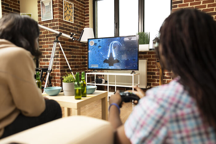 Workers playing a video game at home, escaping from corporate buzzwords and practices.