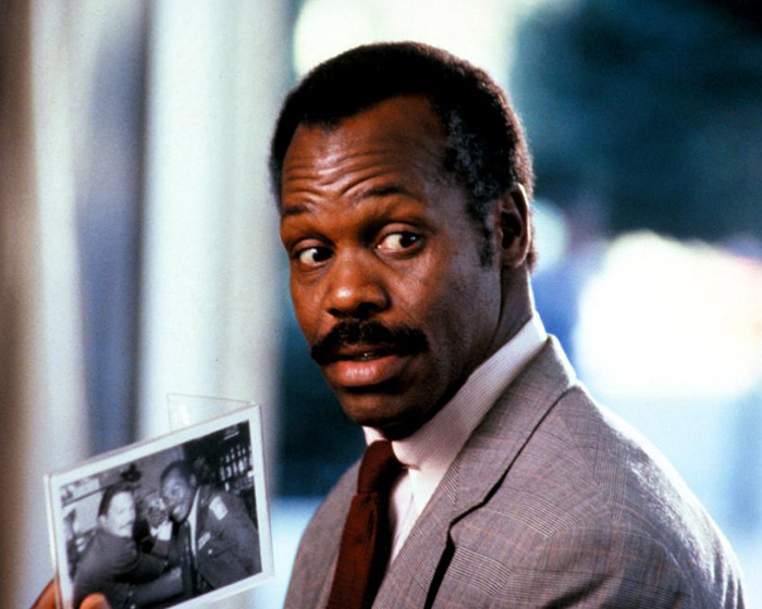 Danny Glover in a suit, holding a photo, looking over his shoulder, with a doctor sharing warning symptoms. Danny Glover in a suit, holding a photo, looking over his shoulder, with a doctor sharing warning symptoms.