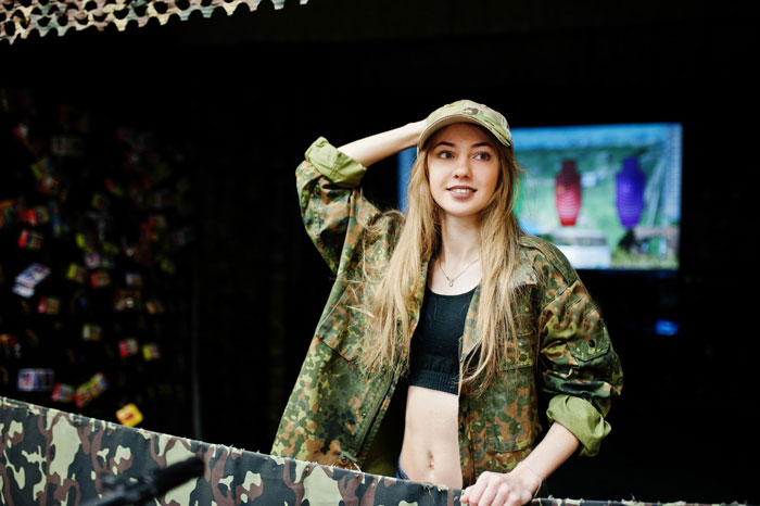 Woman in an Airsoft camouflage jacket and cap, with a target screen in the background, ignoring the dress code. Woman in an Airsoft camouflage jacket and cap, with a target screen in the background, ignoring the dress code.