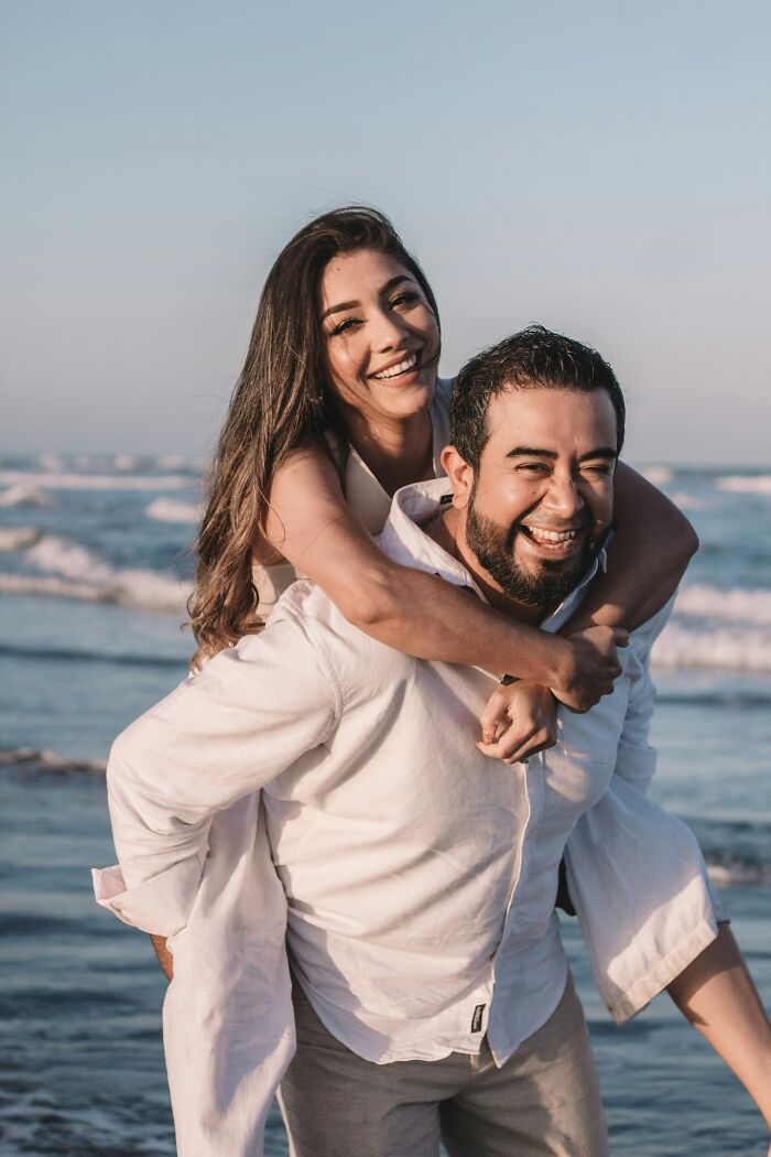 Happy couple getting married, enjoying a piggyback ride on the beach with ocean waves.