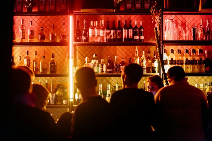A disturbing, dimly lit bar scene with people, showcasing scary bottles of alcohol on shelves.