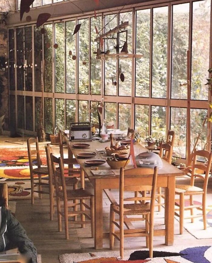 A spacious dining room with a long wooden table and chairs, featuring large windows and a colorful rug, part of remarkable designs and historic interiors.
