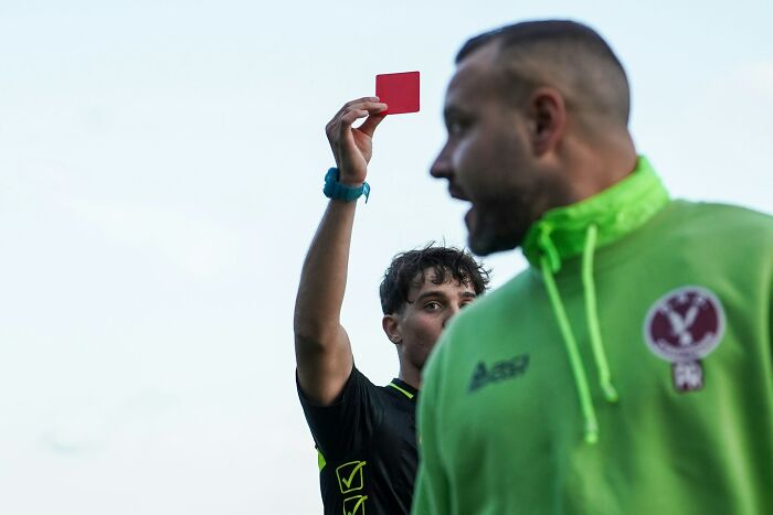 A soccer referee holding up a red card, illustrating American habits vs. British people's expectations.