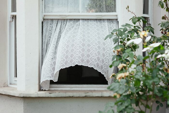 A window with a lace curtain blowing inward, suggesting a chilling atmosphere for babysitting stories.