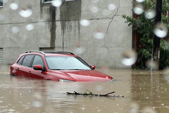 A red vehicle is seen almost completely submerged in water, as a result of the 9/11 attack, with raindrops in the foreground.
