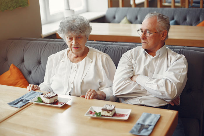 An older couple sitting at a table with desserts, discussing the husband's violent reaction to allergic SIL peanuts. An older couple sitting at a table with desserts, discussing the husband's violent reaction to allergic SIL peanuts.