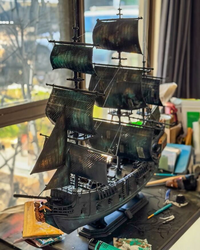 An elaborate pirate ship model, a fantastic 3D printing creation, with dark sails and rigging on a desk.