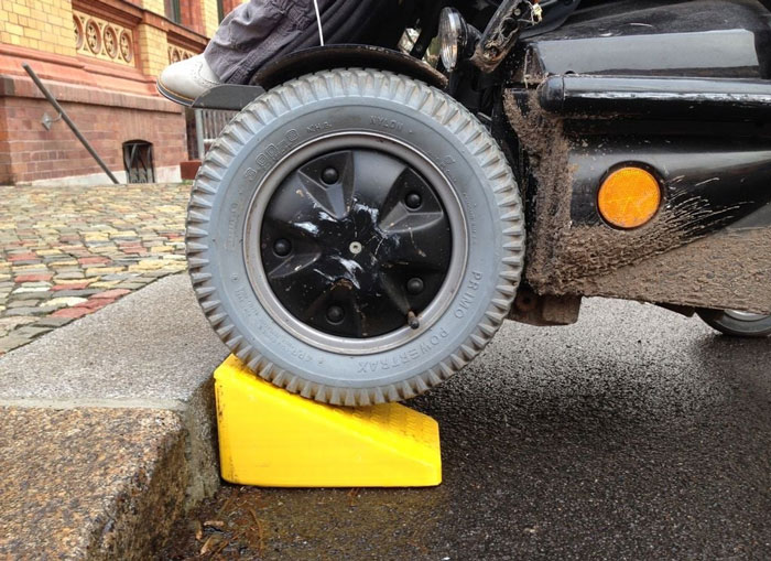 A yellow wedge helping a wheelchair over a curb, demonstrating accessibility in everyday use.