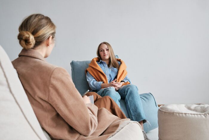 A young woman sits across from her therapist, discussing unhinged therapist moments.