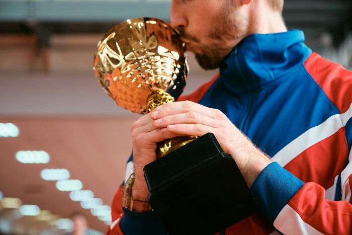 A man in a tracksuit kisses a golden trophy, symbolizing American habits of celebrating success.