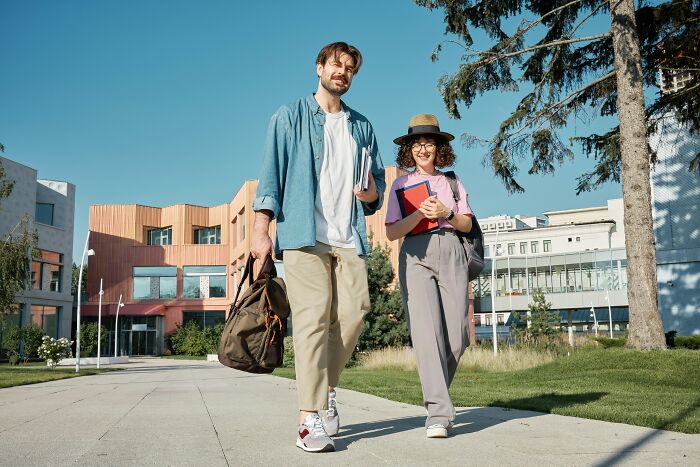 Two students walking on a sunny campus, potentially discussing or encountering mansplaining examples.