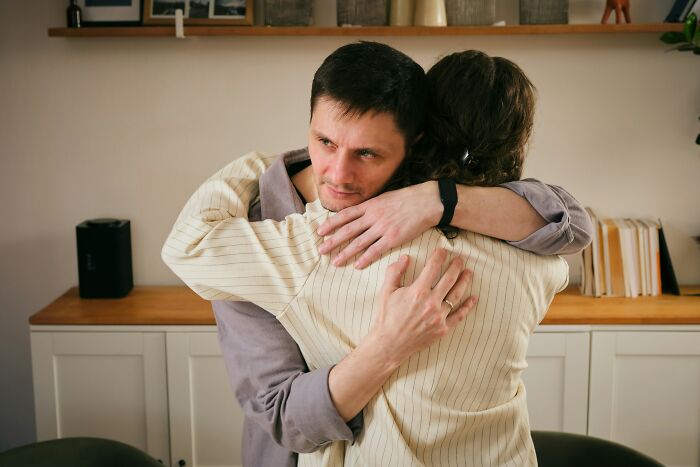 A man with a subtle, unreadable expression while hugging someone, depicting signs someone isn't as nice.
