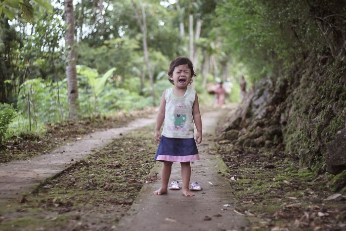 A disturbing image of a crying little girl standing barefoot on a scary dirt path.