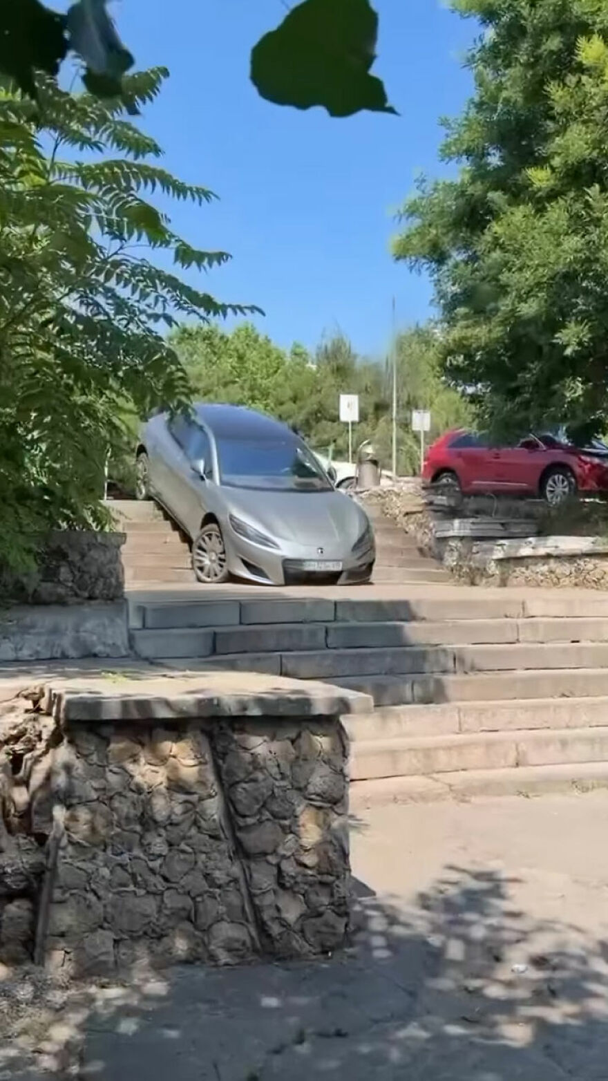 An expensive mistake: a silver car is precariously balanced on a concrete staircase, unable to move.