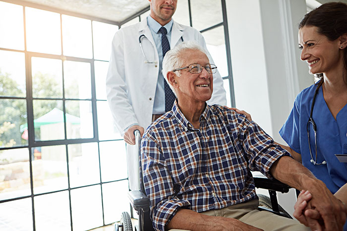 Grandpa in a wheelchair, smiling with a doctor and nurse, illustrating memory care. Grandpa in a wheelchair, smiling with a doctor and nurse, illustrating memory care.