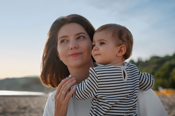 A young mom holding her baby, looking away, with a beach in the background. Mom sides with her son, using autism as an excuse. A young mom holding her baby, looking away, with a beach in the background. Mom sides with her son, using autism as an excuse.