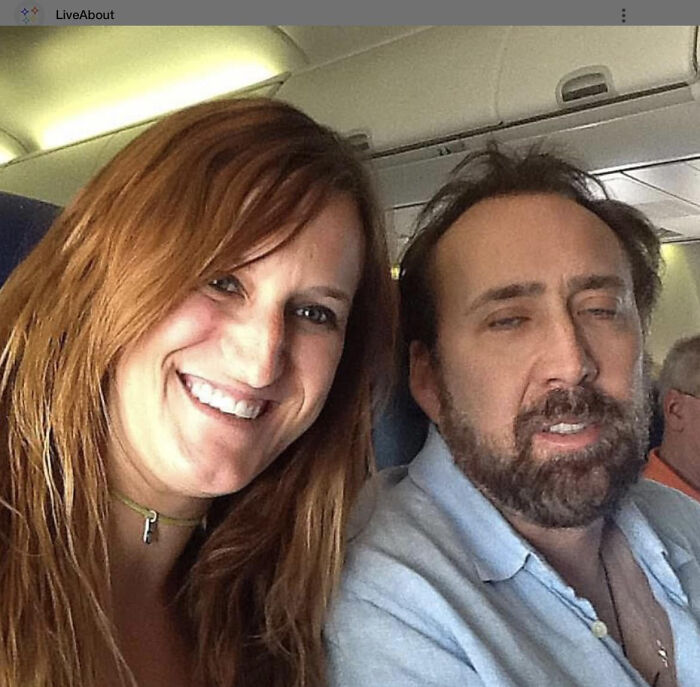 A smiling woman takes a selfie with Nicolas Cage, who appears to be sleeping. A moment people asked celebrities for a photo.