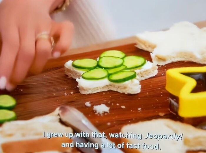 Meghan Markle's hands arranging cucumber slices on a star-shaped sandwich, referencing her upbringing and fast food. Meghan Markle's hands arranging cucumber slices on a star-shaped sandwich, referencing her upbringing and fast food.